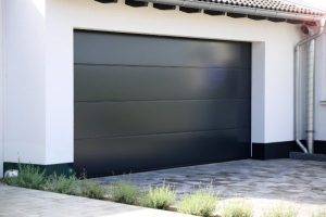 A sleek, dark gray sectional garage door on a modern white house with a brick driveway.
